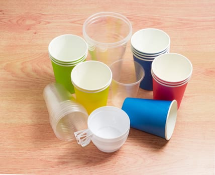 Different disposable transparent and white plastic cups, disposable paper cups in red, green, blue and yellow colors on a wooden surface
