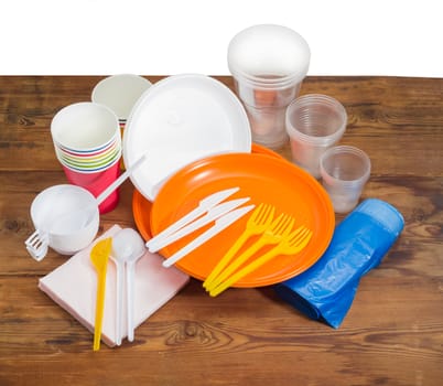 Different disposable plastic and paper cutlery, paper napkins and roll of disposable garbage bags on the old wooden planks 
