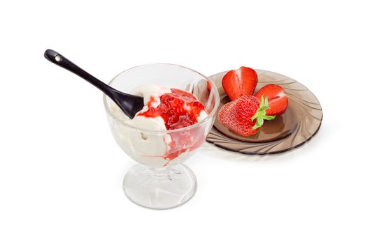 Ice cream poured on with mashed fresh strawberry, black ceramic teaspoon in glass for ice cream and two halves and one whole of a fresh strawberry on glass saucer on a light background