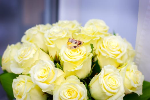 Wedding rings lie on a wedding bouquet from roses