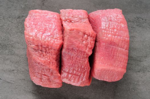 three pieces of fresh pink raw beef meat places at shale board, top view