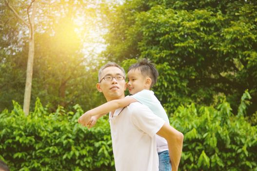 Asian father giving piggyback ride to his son in the evening sunshine