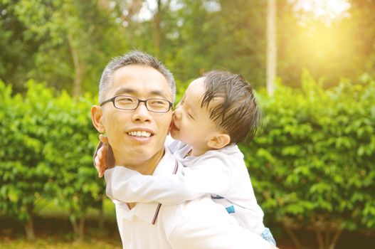 Asian father giving piggyback ride to his son in the evening sunshine