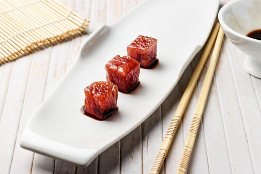 Tuna sashimi dipped in soy sauce with chopsticks and bamboo mat. Raw fish in traditional Japanese style. Horizontal image.