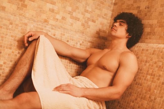 Handsome young muscular man relaxing in the steam bathroom at the spa centre.
