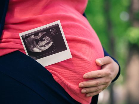 Close up view of ultrasound scan and pregnant tummy. Hand on belly