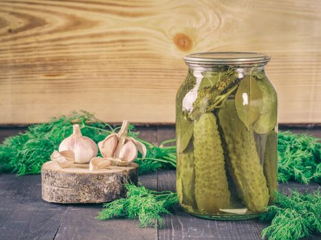 Pickled cucumbers on wooden background. Pickles in glass jar with garlic and fresh dill. Salted cucumber in jar with copy space