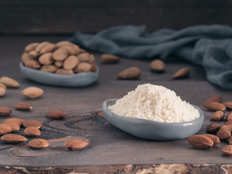 Almond powder in gray trendy plate and almonds on dark wooden table. Almond flour and peeled kernel almonds. Copy space.