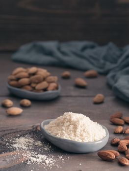 Almond powder in gray trendy plate and almonds on dark wooden table. Almond flour and peeled kernel almonds. Copy space. Vertical.