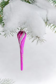 Pink Christmas toy on a fir branch covered with snow outdoors