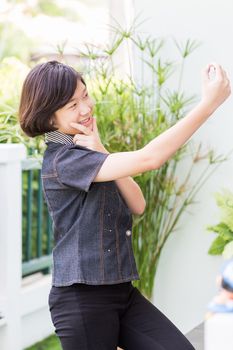 Asian girl with short hair using mobile phone to take selfie outdoor in garden