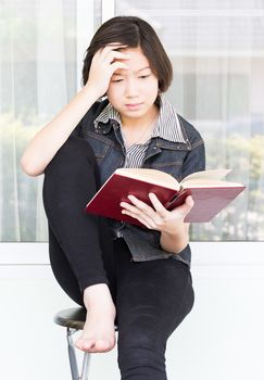 Asian girl with short hair reading a book sitting on a chair