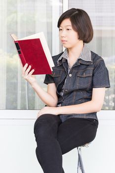 Asian girl with short hair reading a book sitting on a chair