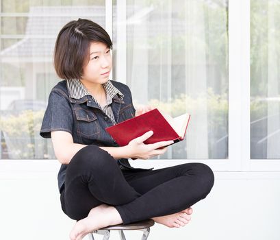 Asian girl with short hair reading a book sitting on a chair