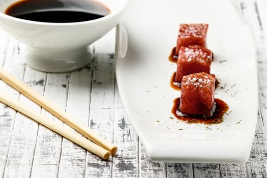 Tuna sashimi dipped in soy sauce,  thick salt and dill on old white wooden board with chopsticks and sauce bowl. Raw fish in traditional Japanese style. Horizontal image.