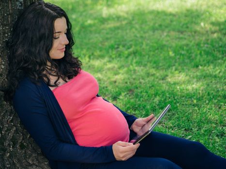 Pregnant woman with tablet or e-reader outdoors. Copy space.
