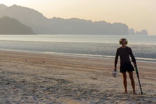 a treasure hunter with Metal detector on sunrise on the beach