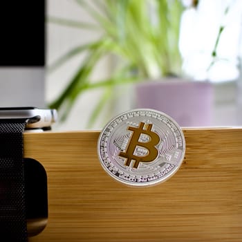 Cryptocurrency physical silver bitcoin coin on the wooden holder near watch.