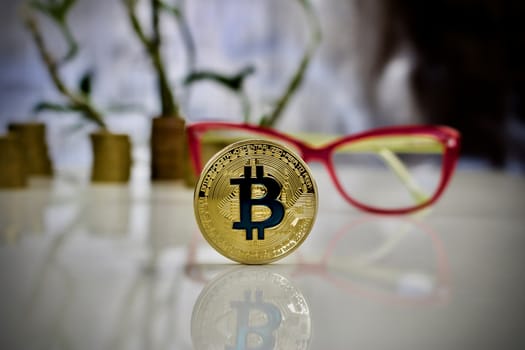 Digital currency physical gold bitcoin coin with blue sign near pink glasses