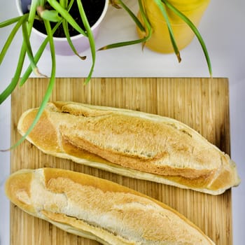 Fresh bread on the wooden kitchen board near green flowers and bottle.
