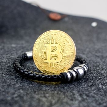 Cryptocurrency gold bitcoin coin and black bracelet with a silver decoration