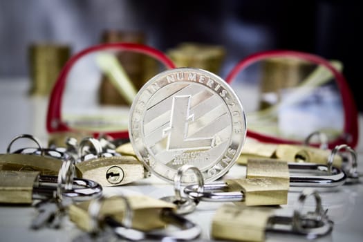 Cryptocurrency physical silver litecoin coin near gold padlocks and pink glasses