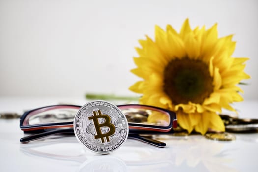 Bitcoin concept. Digital cryptocurrency physical coin with sunflower and glasses.