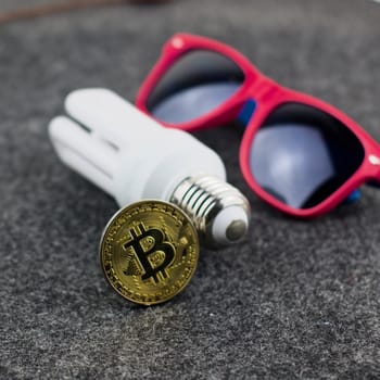 Cryptocurrency physical bitcoin coin concept. Pink sunglasses and eco bulb.