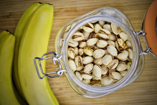 Pistachio nuts in jar and yellow bananas on the wooden board