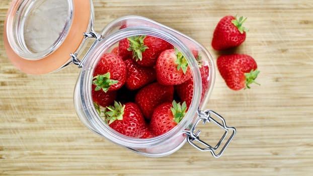 Fresh red strawberries in big kitchen jar on the wooden board.