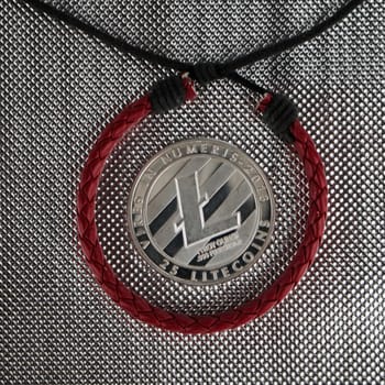Cryptocurrency physical silver litecoin coin near red skin bracelet. Finance concept.
