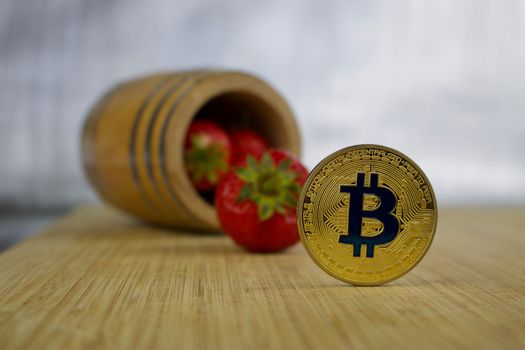 Cryptocurrency physical gold bitcoin coin near barrel with strawberries