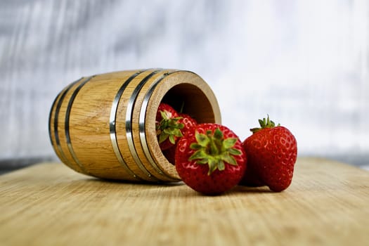 Wooden barrel on the wooden board and red fresh strawberries.