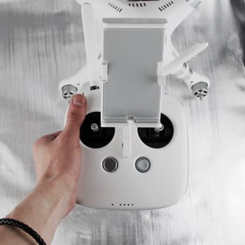 White big drone controller in hand near white quadcopter.