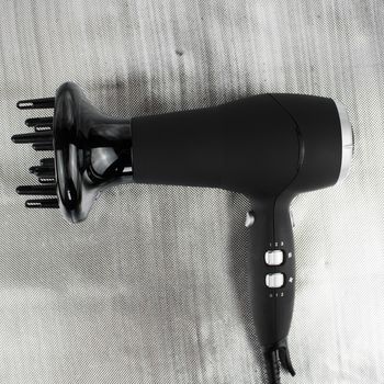Big black proffesional hair dryer on the silver background with a silver buttons.