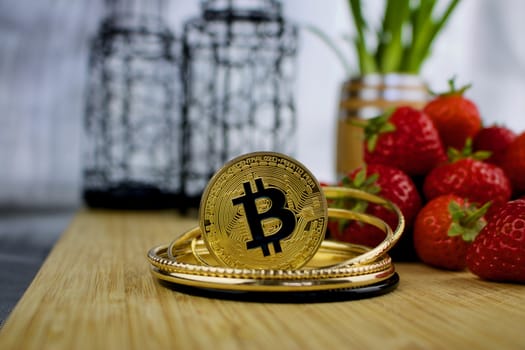 Digital currency physical gold bitcoin coin near strawberries. Fruit concept.