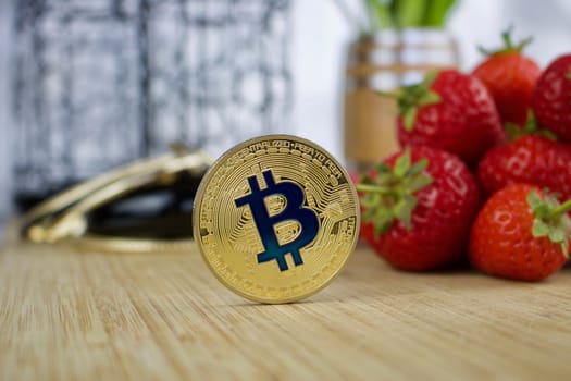 Cryptocurrency physical gold bitcoin coin near red strawberries.