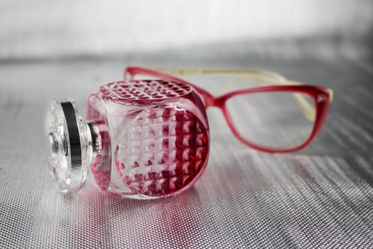 Pink bottle with a perfume and pink female glasses