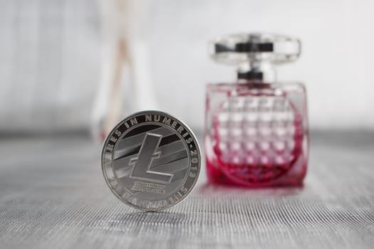 Digital currency silver litecoin coin near pink fragrance in luxury bottle