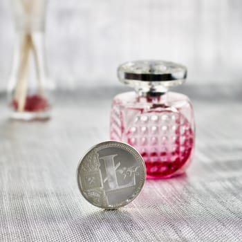 Digital currency physical silver litecoin coin near pink fragrance bottle.