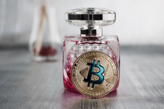 Cryptocurrency physical gold bitcoin coin near pink fragrance bootle.