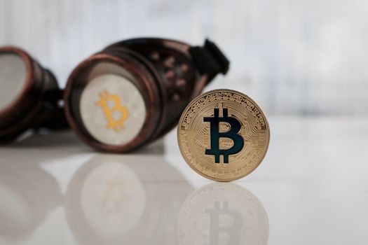 Cryptocurrency physical gold and silver bitcoin coin near steampunk glasses.