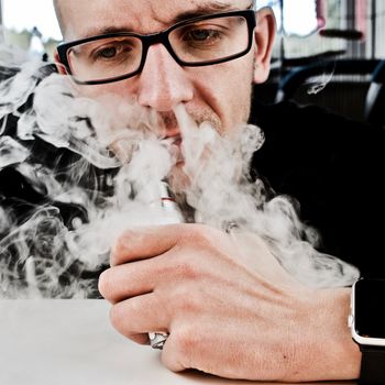 Young man in black scene smoking electronic cigarette. Vape.