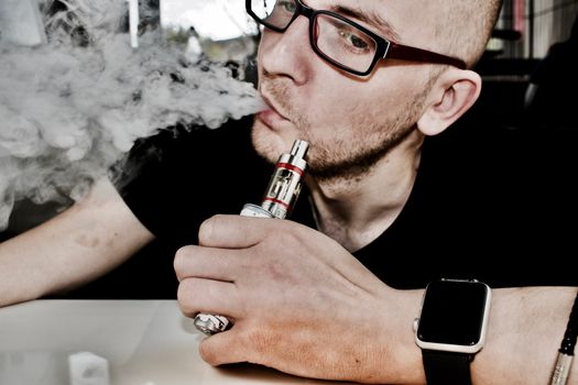 Young man in glasses smoking electronic cigarette.