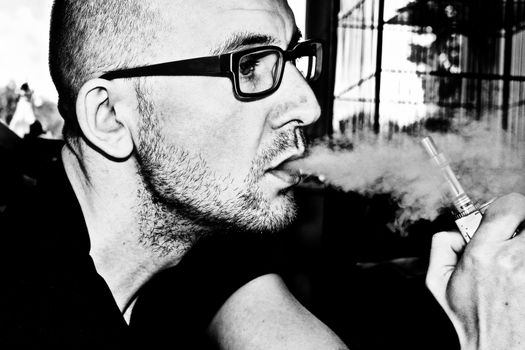 Young man in black glasses smoking electronic cigarette