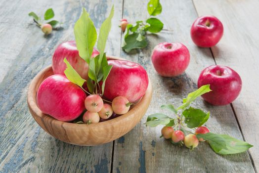 Several red apples with green leaves lie in a wooden bowl on the old wooden table