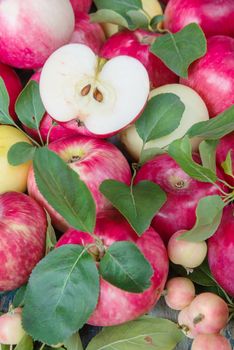 Many red apples with green leaves and half of apple on the old wooden table