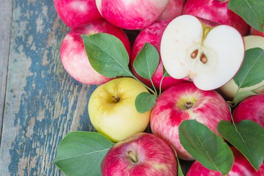 Many red apples with green leaves on the old wooden table