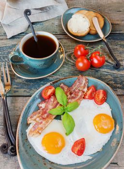 Breakfast consists of fried eggs,  bacon, tomato, toast and a cup of coffee on the old wooden table; top view, flat lay