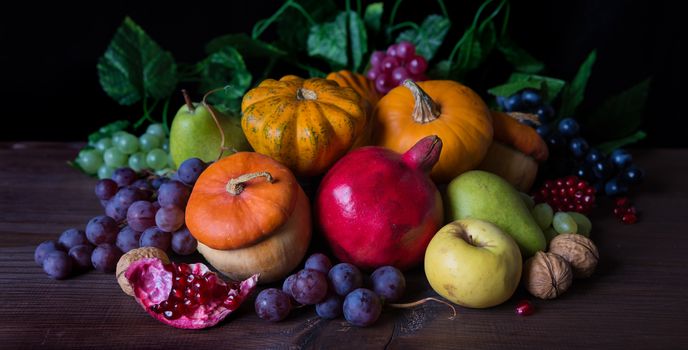 Autumn still life: decorative pumpkins, squash, apples, pears, pomegranates and grapes on the dark wooden background